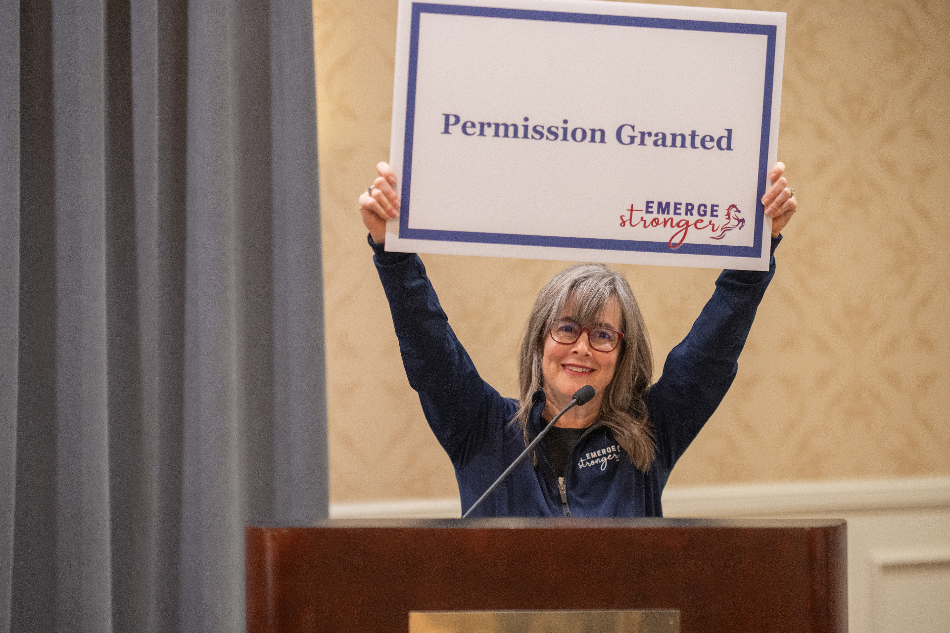 Physician holding a 'Permission Granted' sign at an Emerge Stronger event
